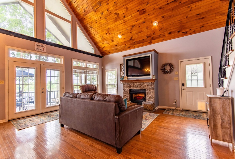 Living room featuring high vaulted ceiling, light wood-style flooring, a stone fireplace, french doors, and wooden ceiling