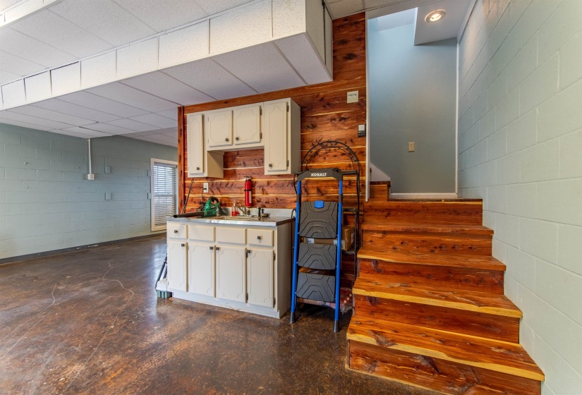 Garage wet bar with concrete block wall, white cabinets, light countertops, concrete floors, and a paneled ceiling
