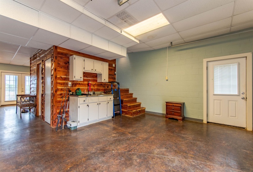 Garage living area featuring a paneled ceiling, french doors, concrete block wall, and white cabinets