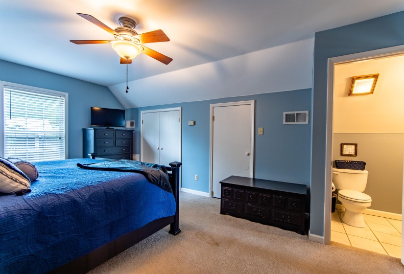 Carpeted bedroom with two closets, vaulted ceiling, ceiling fan, tile patterned floors, and ensuite bathroom