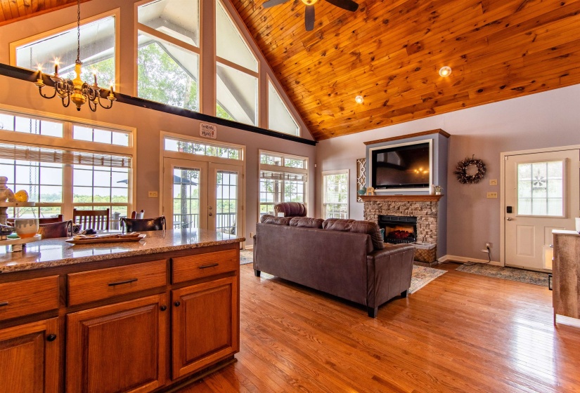 Living area featuring high vaulted ceiling, light wood-style floors, a fireplace, wooden ceiling, and a ceiling fan