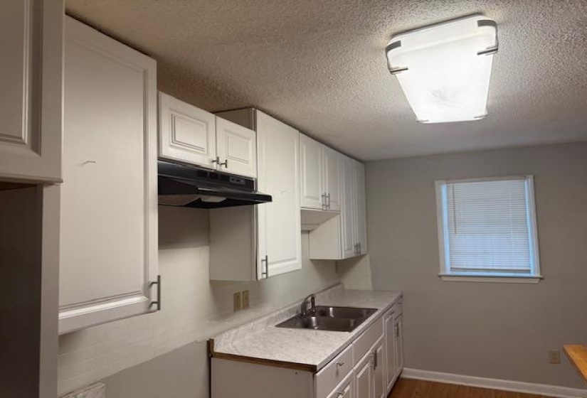 Kitchen featuring under cabinet range hood, light countertops, white cabinets, wood finished floors, and a textured ceiling