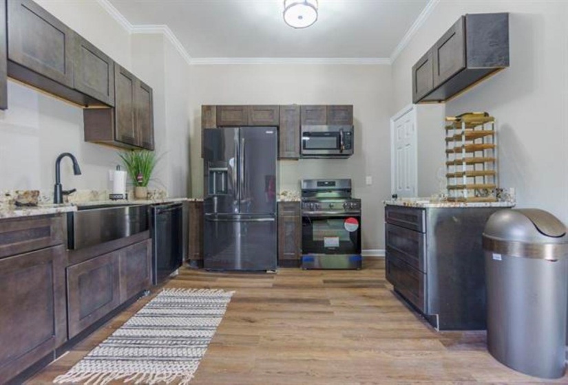 Kitchen with appliances with stainless steel finishes, crown molding, light wood finished floors, dark brown cabinetry, and light stone counters