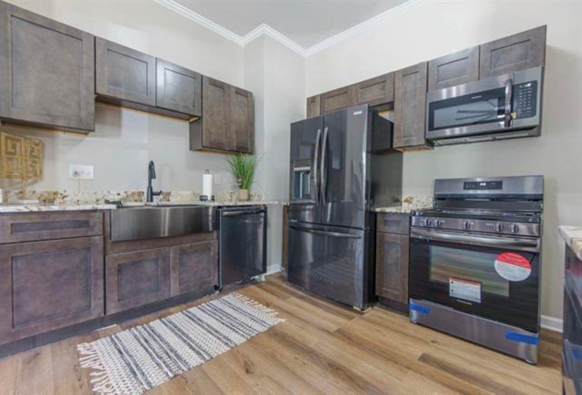 Kitchen featuring appliances with stainless steel finishes, crown molding, dark brown cabinetry, light wood-style floors, and light stone counters