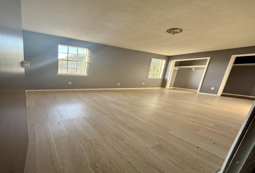 Unfurnished bedroom with two closets, light wood-style floors, and a textured ceiling