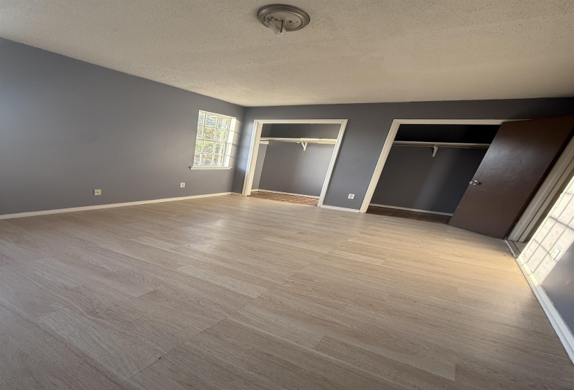 Unfurnished bedroom featuring two closets, a textured ceiling, and light wood finished floors