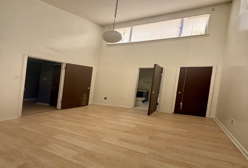 Empty room with a high ceiling, a textured ceiling, and light wood-style floors