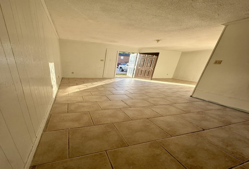 Empty room with a textured ceiling, light tile patterned floors, and wooden walls