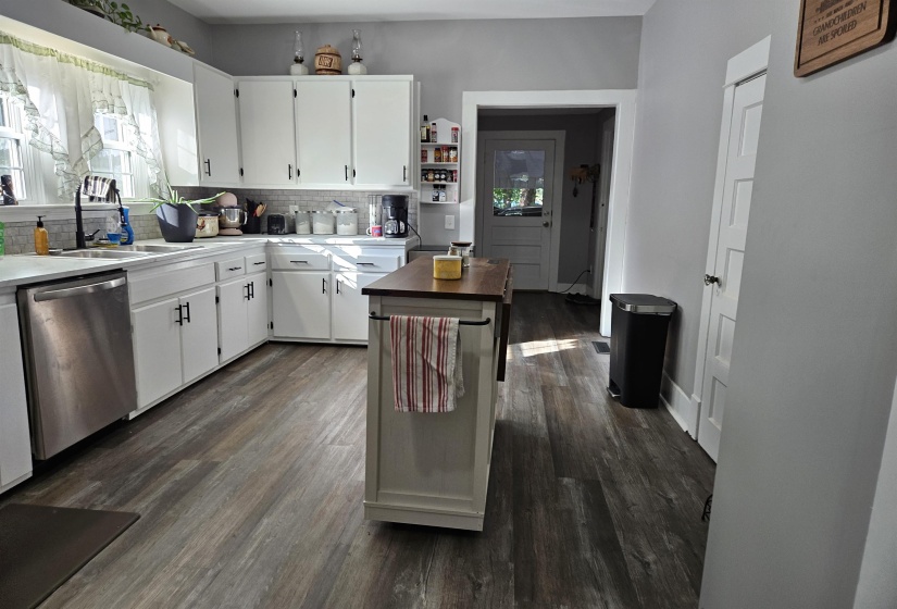 Kitchen with white cabinets, decorative backsplash, stainless steel dishwasher, and dark wood-style floors