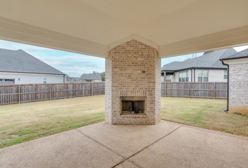 Fenced backyard with an outdoor brick fireplace and a patio area