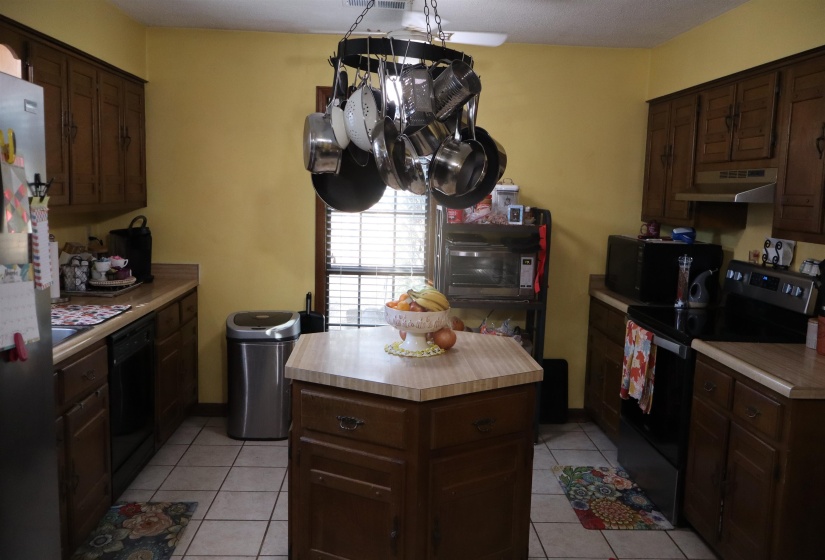 Kitchen featuring black appliances, light tile patterned flooring, dark brown cabinetry, under cabinet range hood, and light countertops