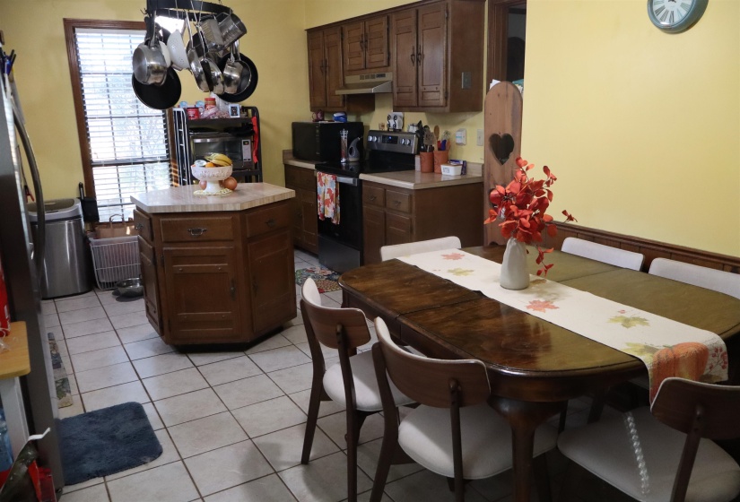 Kitchen with black appliances, light tile patterned floors, dark brown cabinetry, a kitchen island, and under cabinet range hood