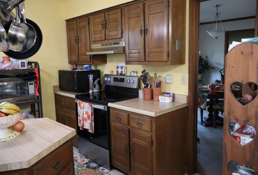 Kitchen with electric range, light countertops, black microwave, under cabinet range hood, and brown cabinetry