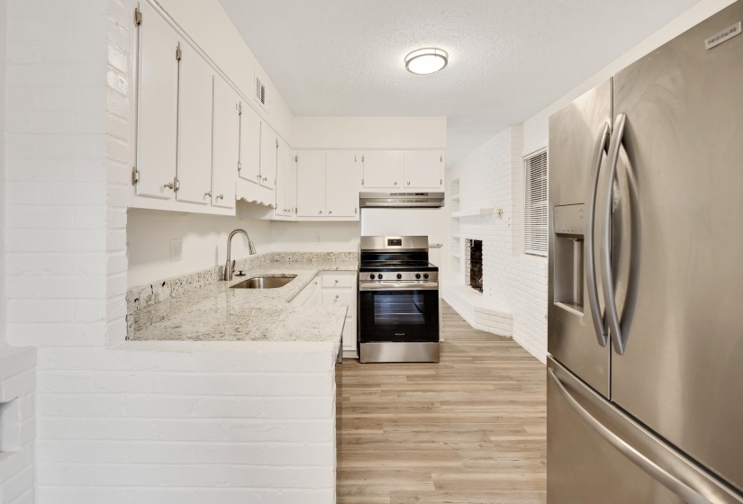 Kitchen featuring appliances with stainless steel finishes, light stone counters, light wood-type flooring, a textured ceiling, and white cabinets