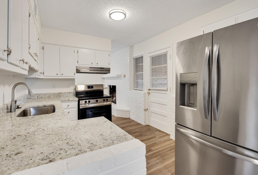 Kitchen with stainless steel appliances, a textured ceiling, light wood-style floors, white cabinets, and light stone counters