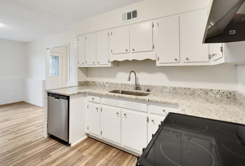 Kitchen featuring black / electric stove, extractor fan, light stone counters, white cabinetry, and wainscoting