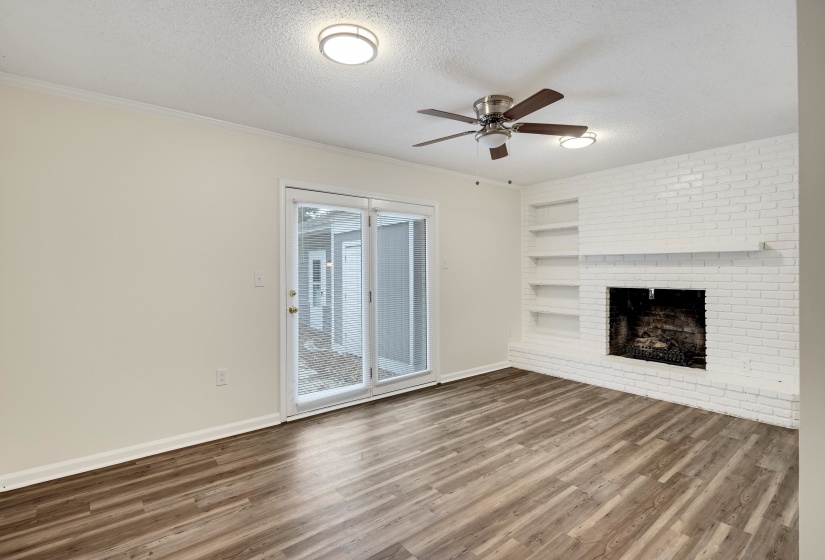 Unfurnished living room featuring a textured ceiling, wood finished floors, ceiling fan, a brick fireplace, and ornamental molding
