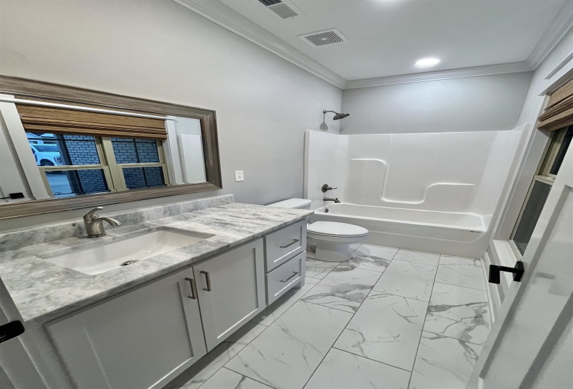 Full bathroom with vanity, ornamental molding,  shower combination, and light marble finish flooring
