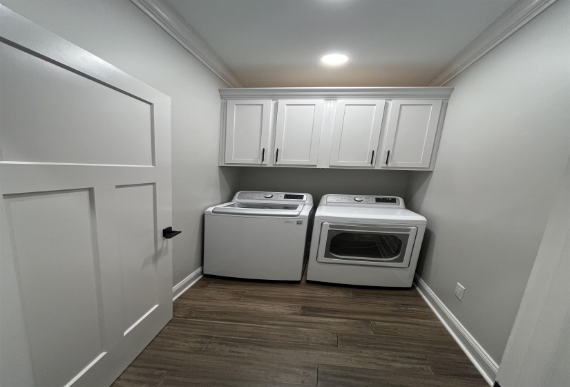 Washroom with dark wood finished floors, cabinet space, ornamental molding, and washer and clothes dryer