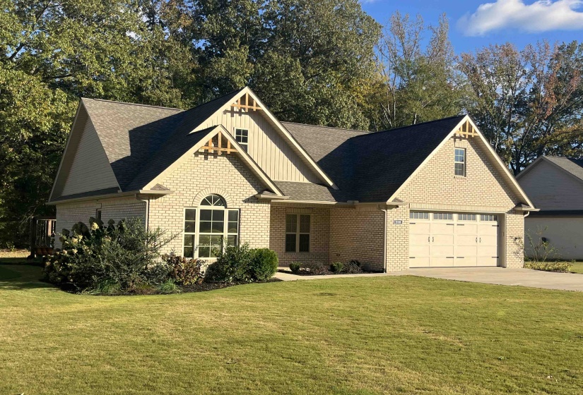 Craftsman-style home with board and batten siding, a front lawn, driveway, brick siding, and roof with shingles