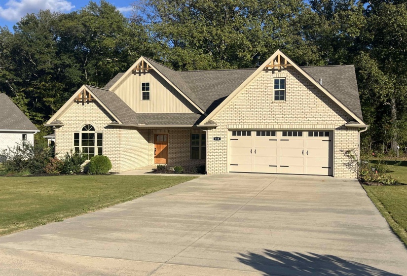 View of front facade featuring brick siding, driveway, roof with shingles, board and batten siding, and a front lawn