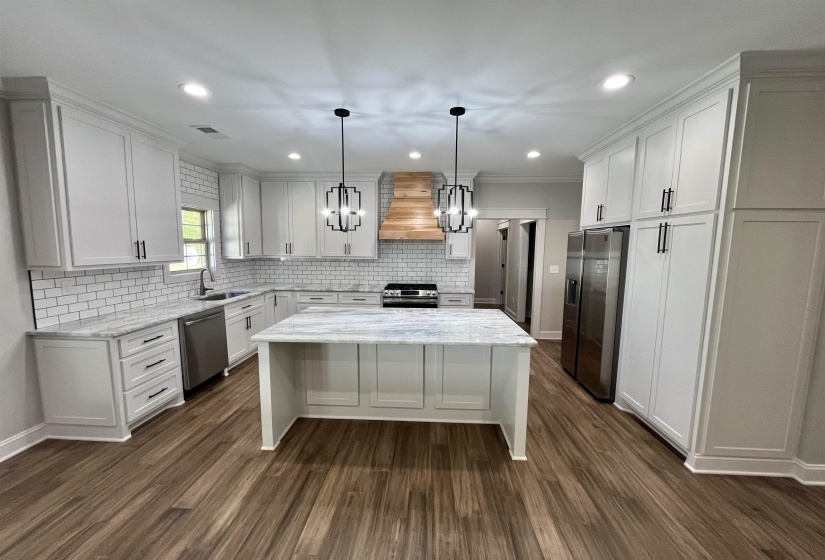 Kitchen with pendant lighting, light stone countertops, appliances with stainless steel finishes, a kitchen island, and white cabinets
