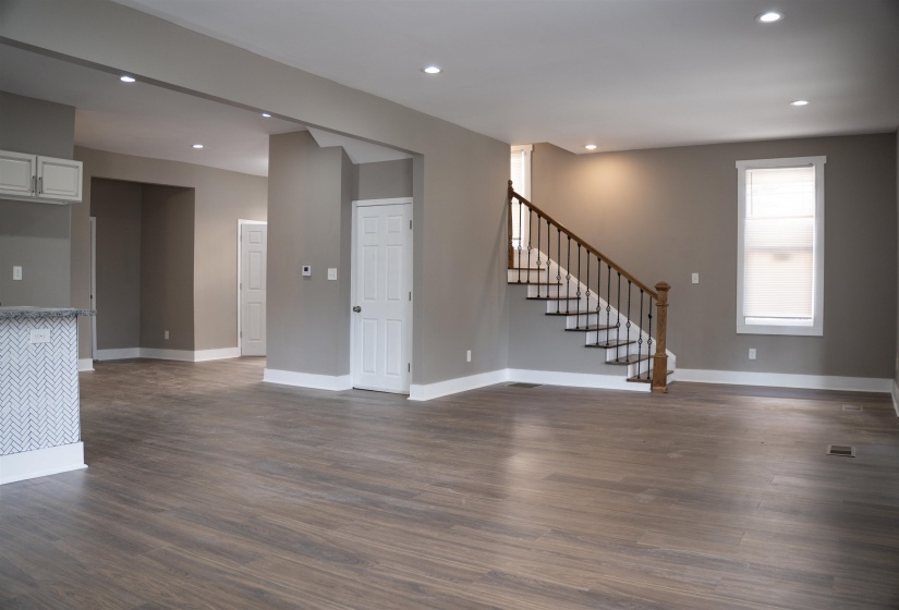 Unfurnished living room featuring recessed lighting, dark wood-type flooring, and stairway