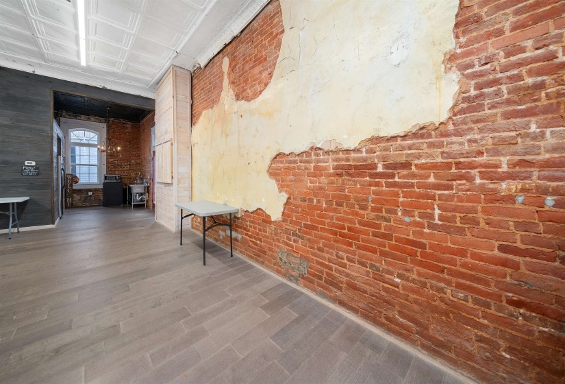 Hall with brick wall, wood finished floors, an ornate ceiling, and a chandelier