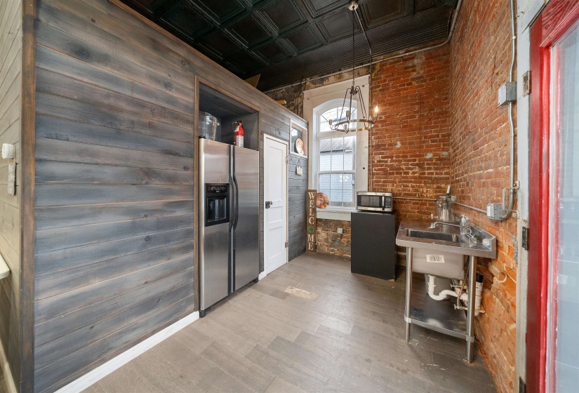 Kitchen featuring wood finished floors, appliances with stainless steel finishes, an ornate ceiling, brick wall, and open shelves