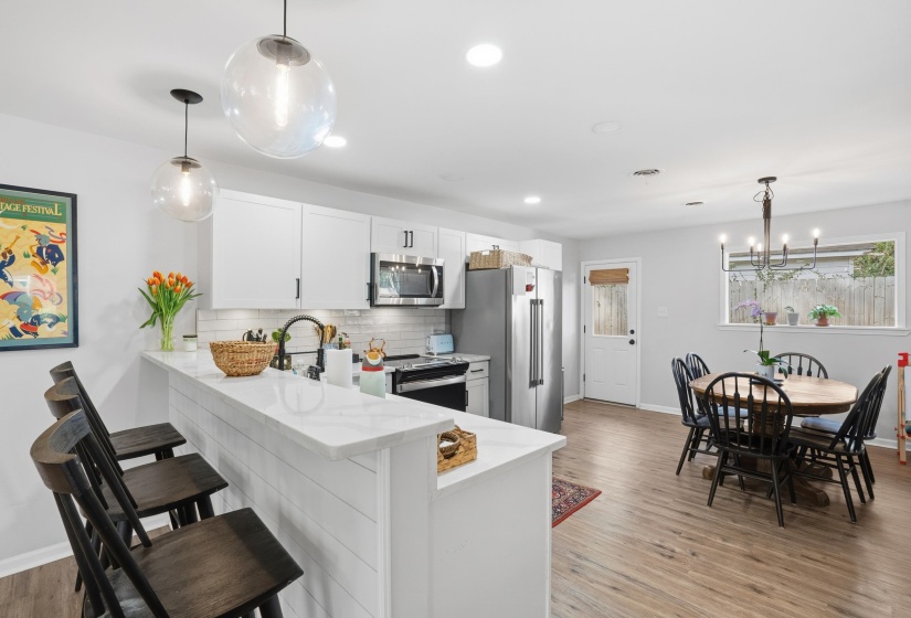 Kitchen featuring decorative light fixtures, light stone countertops, decorative backsplash, white cabinetry, and a peninsula