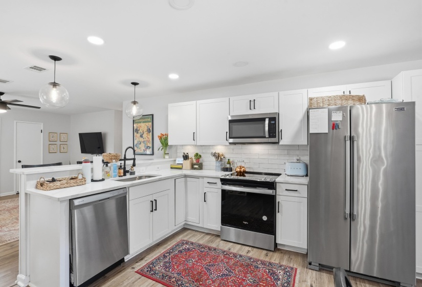 Kitchen featuring appliances with stainless steel finishes, a peninsula, white cabinetry, pendant lighting, and backsplash