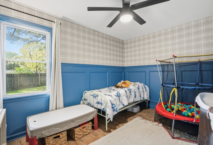 Bedroom with wallpapered walls, a decorative wall, wainscoting, wood finished floors, and ceiling fan