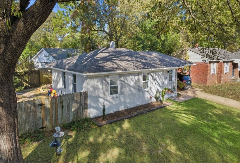 View of side of home with roof with shingles, a chimney, brick siding, and view of scattered trees