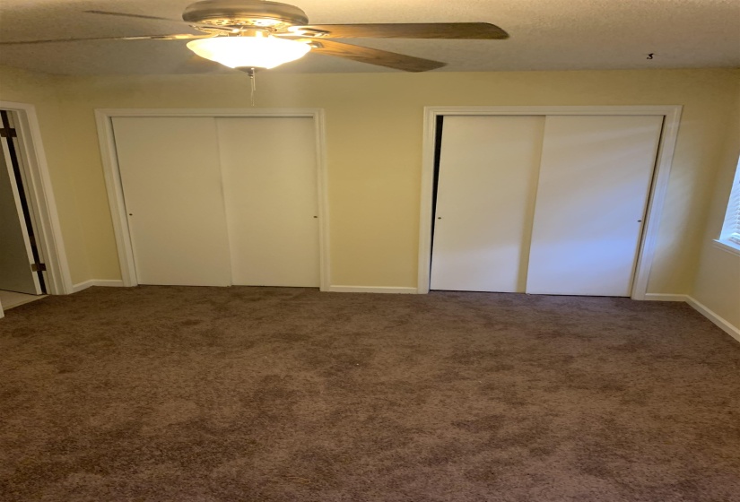 Unfurnished bedroom with two closets, carpet floors, a ceiling fan, and a textured ceiling
