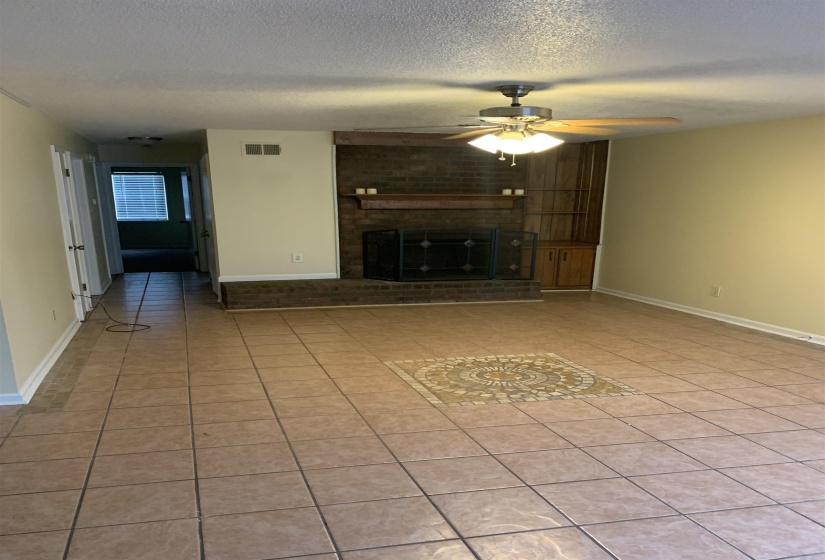 Unfurnished living room with light tile patterned floors, a textured ceiling, ceiling fan, and a brick fireplace