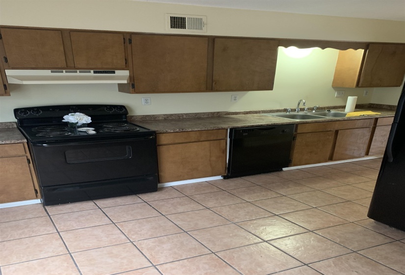 Kitchen with black appliances, light tile patterned floors, under cabinet range hood, brown cabinets, and dark countertops