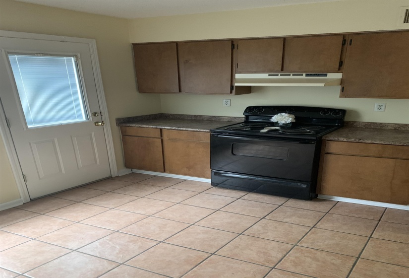 Kitchen with electric range, dark countertops, light tile patterned flooring, and under cabinet range hood
