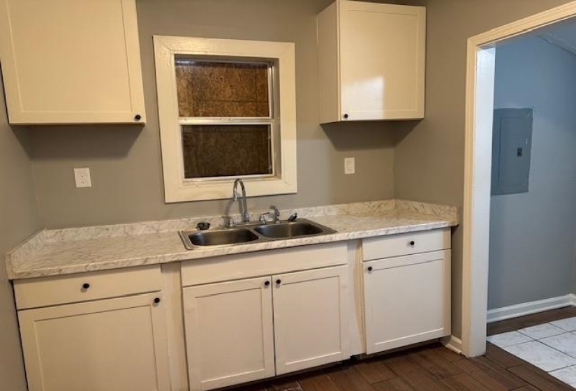 Kitchen featuring white cabinetry, dark wood-type flooring, baseboards, a sink, and electric panel