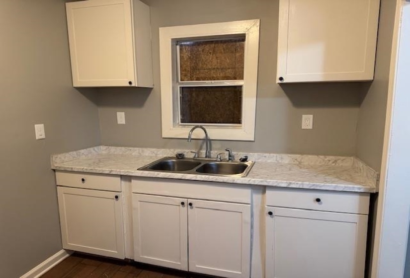 Kitchen with baseboards, dark wood-style flooring, white cabinets, and a sink