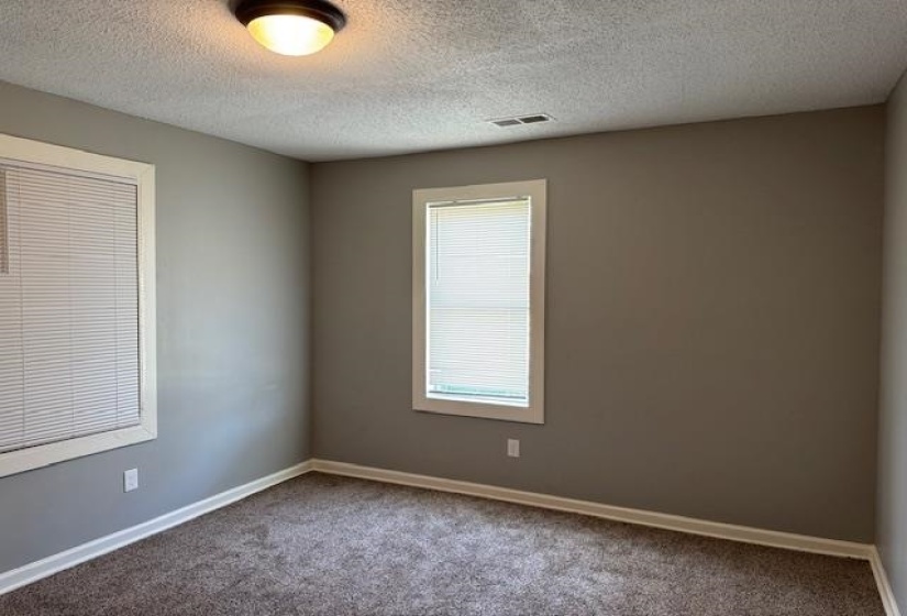 Carpeted spare room with baseboards, a textured ceiling, and visible vents