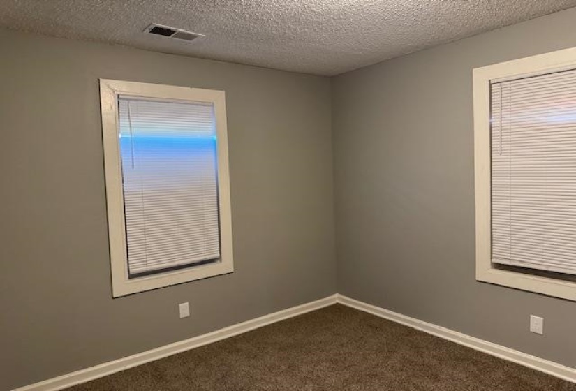 Empty room featuring baseboards, dark carpet, a textured ceiling, and visible vents