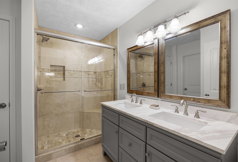 Full bathroom featuring a textured ceiling, a shower stall, double vanity, and light tile patterned floors