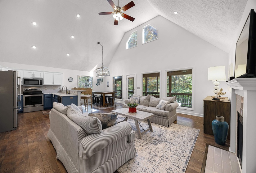 Living room with high vaulted ceiling, dark wood-style flooring, a ceiling fan, a chandelier, and a fireplace with flush hearth