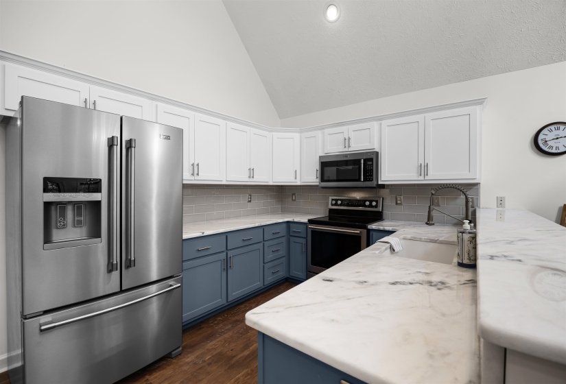 Kitchen featuring blue cabinetry, stainless steel appliances, white cabinets, tasteful backsplash, and light stone counters