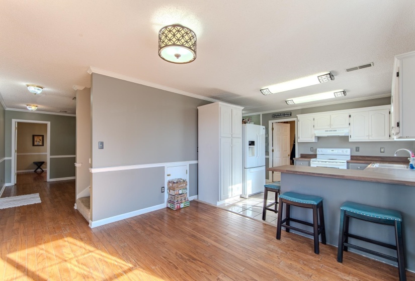 Kitchen featuring crown molding, a peninsula, white cabinets, white appliances, and a breakfast bar