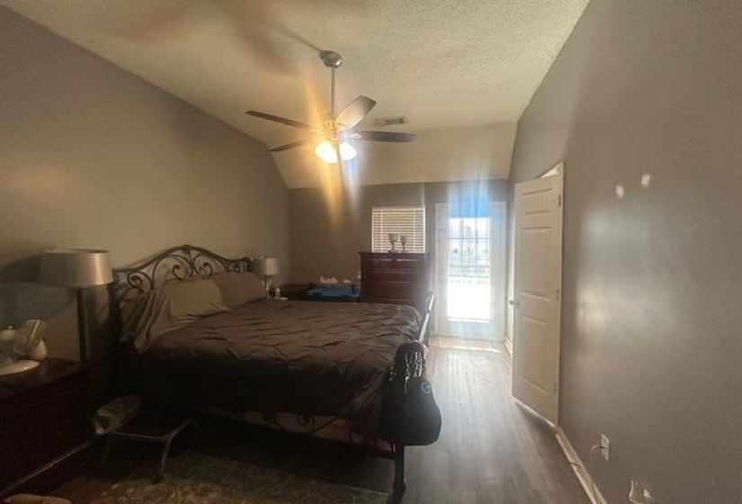 Bedroom with wood finished floors, vaulted ceiling, a ceiling fan, and a textured ceiling