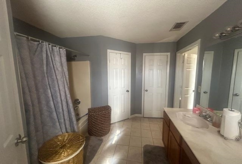 Bathroom with a textured ceiling, shower / bath combination with curtain, vanity, and light tile patterned floors
