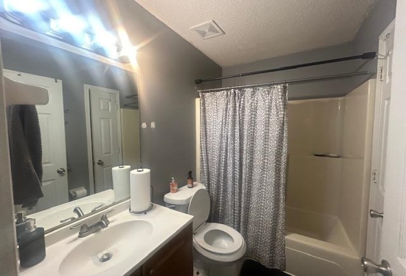 Bathroom featuring a textured ceiling, vanity, and shower / bathtub combination with curtain
