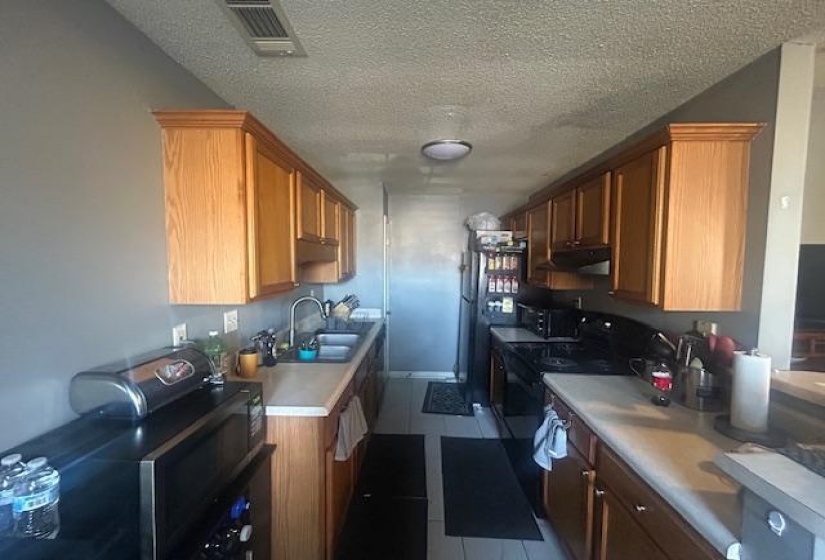 Kitchen featuring a textured ceiling, black appliances, light countertops, dark tile patterned floors, and brown cabinets