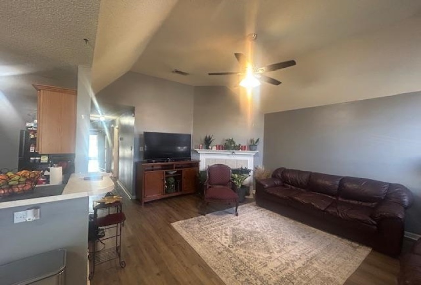 Living room with vaulted ceiling, dark wood-type flooring, a textured ceiling, and ceiling fan